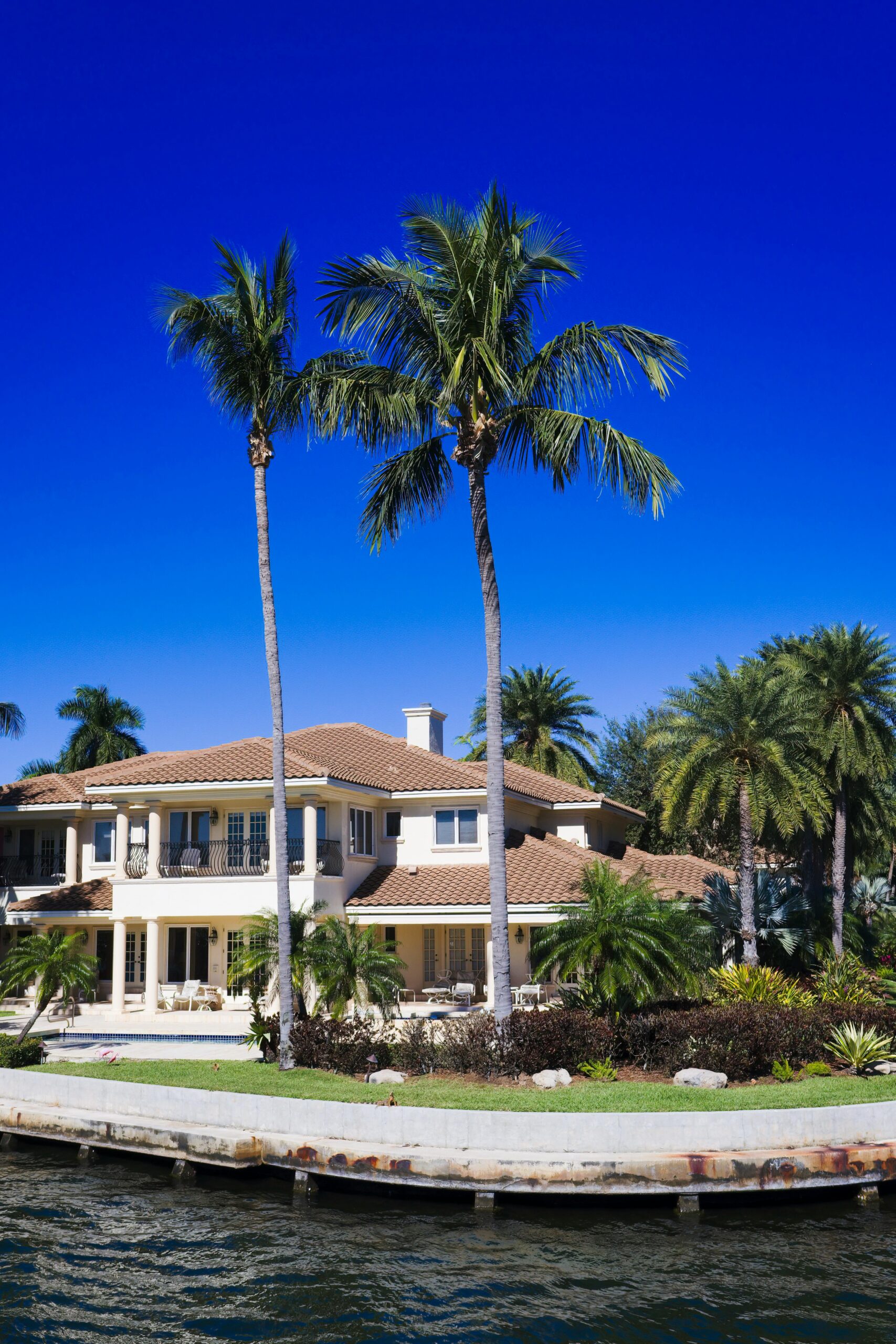 Stunning waterfront home bordered by palm trees under a bright summer sky.