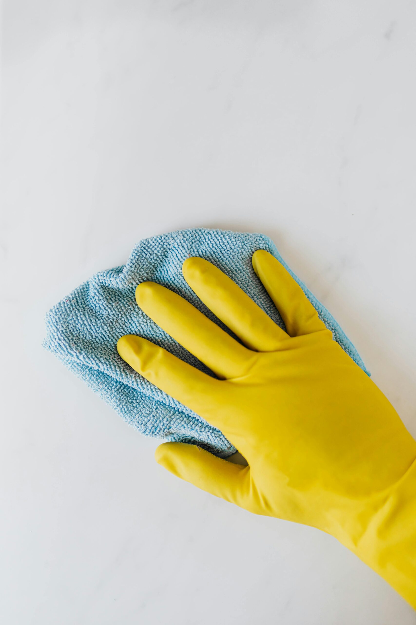Top view of crop anonymous housekeeper in protective gloves cleaning and polishing white surface with blue rag